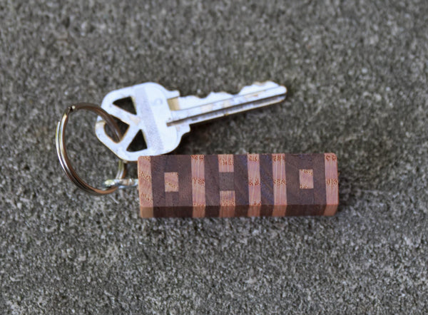 Hand cut letters Ohio keychain in walnut and ash wood. Concrete background. Silver key on keychain.