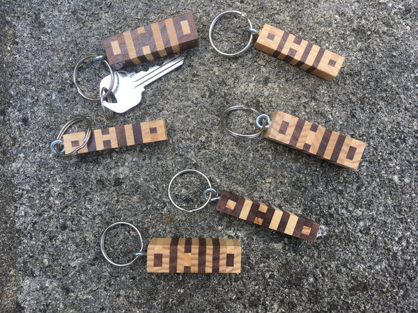 Several Hand cut letters Ohio keychain in walnut and ash wood. Concrete background.