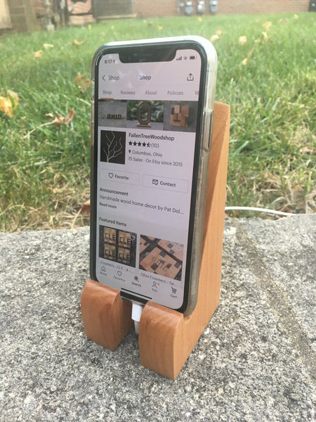 Hand crafted phone stand from fallen cherry, set with a grass background.Shown with an iphone on it's carger.