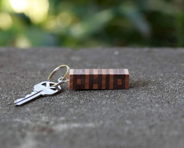Hand cut letters Ohio keychain in walnut and ash wood. Concrete background.Silver key on keychain.