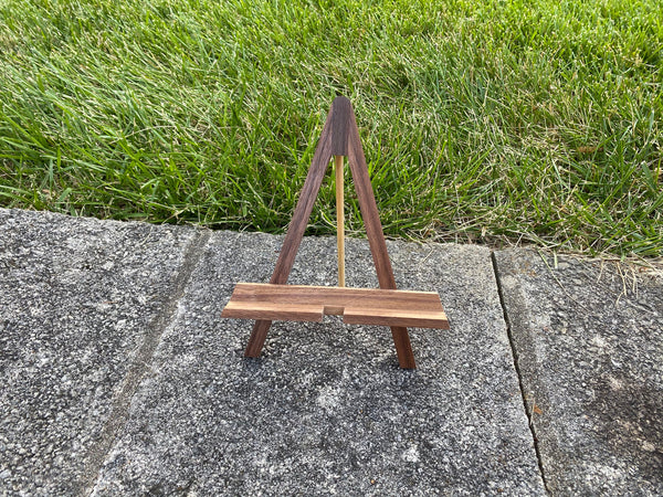 Walnut wood easel phone stand shown on a grass background.