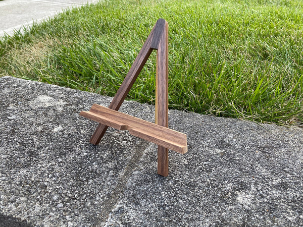 Walnut wood easel phone stand on a grass background.