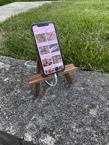 Walnut wood phone stand, easel. Displayed with a phone and charging access.